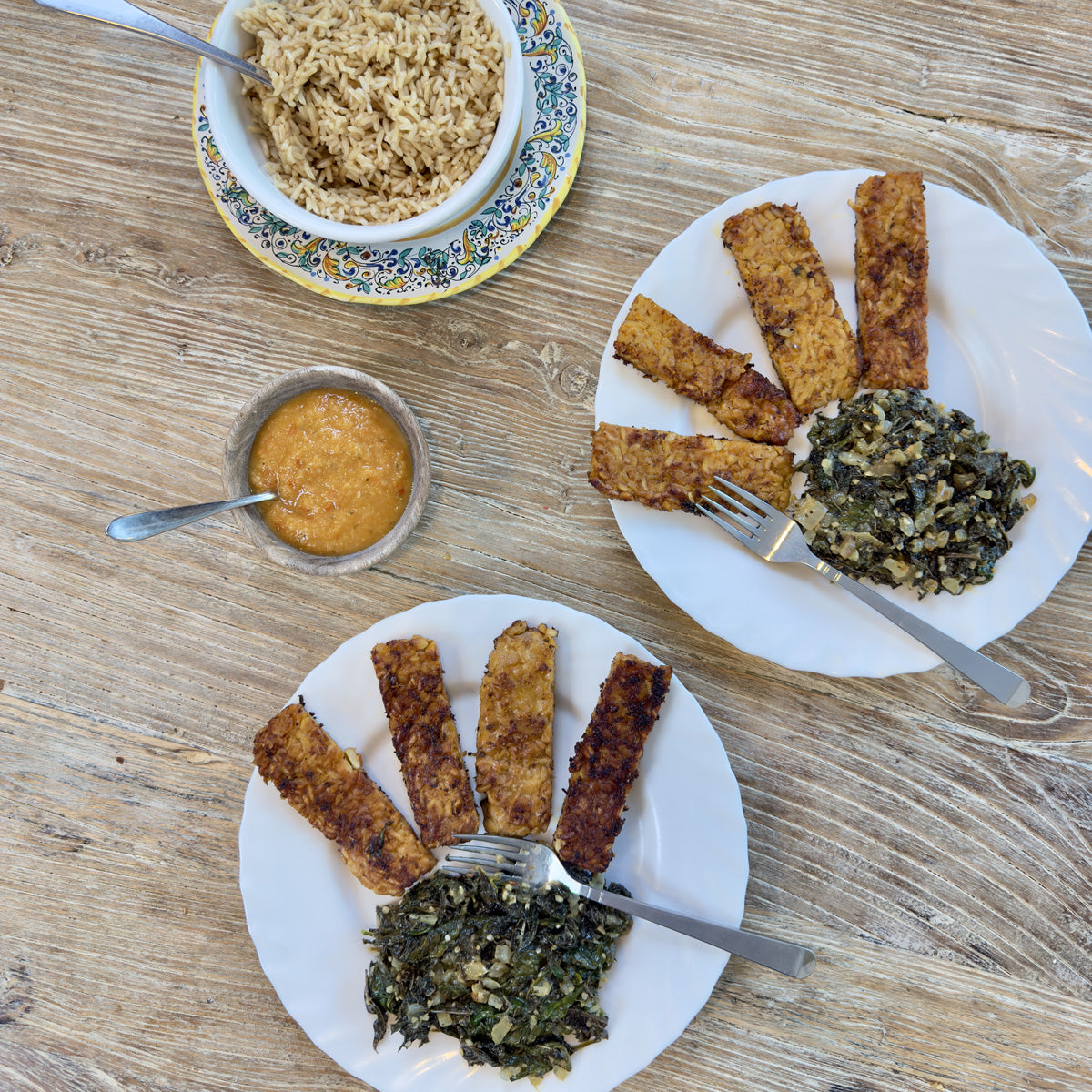 Plates of tempeh and lalo with bowls of haitian epis and rice
